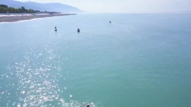 Turkuaz denizin arka planında kürekleri olan sörfçülerin ve açık gökyüzünün üst görüntüsü. Şarjör. İnsanlar sakin güneşli bir havada sahilde SUP sörfü yaparken rahatlar.
