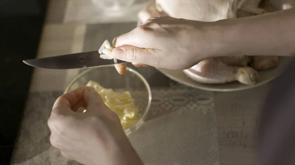 Närbild av honan skära vitlök med en kökskniv. Börja. Ovanifrån av kvinna händer skära vitlök och kasta den i glaset djup tallrik står på bordet, matlagning koncept. — Stockfoto
