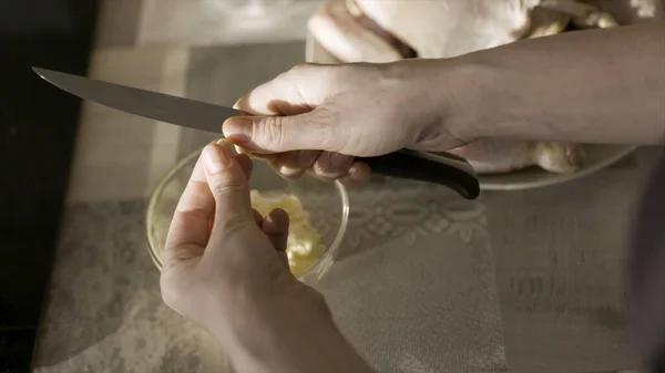 Närbild av honan skära vitlök med en kökskniv. Börja. Ovanifrån av kvinna händer skära vitlök och kasta den i glaset djup tallrik står på bordet, matlagning koncept. — Stockfoto