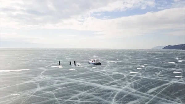 Grupo de personas de pie en el lago de hielo rajado cerca de aerodeslizador. Clip. La gente viaja y explora el lago congelado Baikal en un aerodeslizador seguro y cómodo . — Foto de Stock