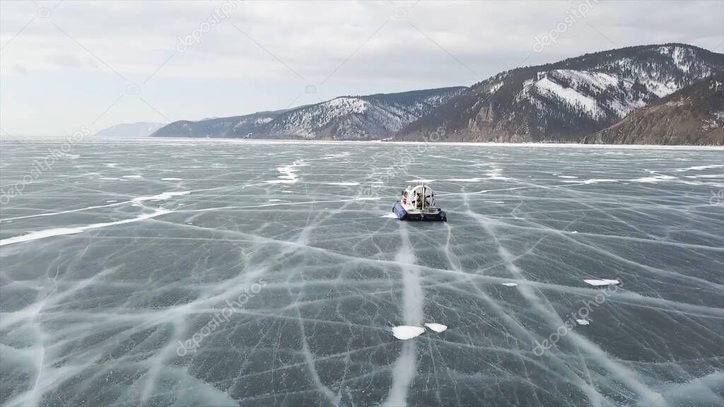 Khivus hovercraft rides on the frozen Lake Baikal. Clip. Aerial view of a hovercraft moving on the ice of a frozen reservoir in winter time on breathtaking snowy hills and cloudy sky background.