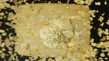 Tahıllı ve tohumlu ev yapımı ekmek hamuru. Stok görüntüleri. Siyah arka planda izole edilmiş hamur üzerine düşen pek çok pulun ve tohumun üst görüntüsü, yemek pişirme kavramı.