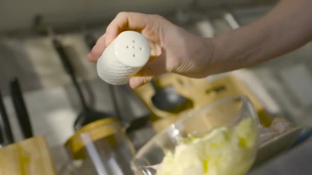 Il sale viene versato nella ciotola. Azione. Il sale di primo piano è aggiunto a boccia con riempitura per piatto. Salare i piatti in cucina casalinga. Il sale in quantità moderate dà il gusto ricco di piatto — Video Stock