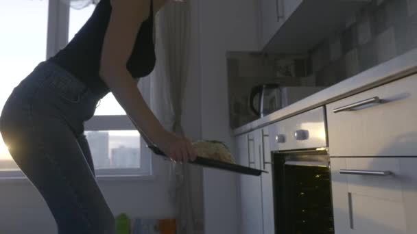 Aantrekkelijke vrouw kookt kip. Actie. Sexy vrouw zet gepekelde kip in de oven op de achtergrond van het avondraam. Mooie vrouw kookt met passie thuis — Stockvideo