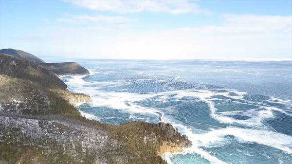 Veduta aerea del lago coperto di ghiaccio e colline innevate di montagna e alberi. Clip. Paesaggio naturale nella stagione invernale, montagne boscose e incredibile lago ghiacciato blu . — Foto Stock