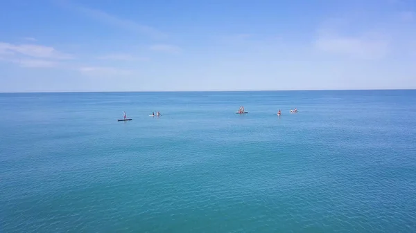 Group of people swim on SUP Board. Clip. Beautiful seascape with people resting on water with SUP boards. Top view of turquoise sea with people on swimming boards