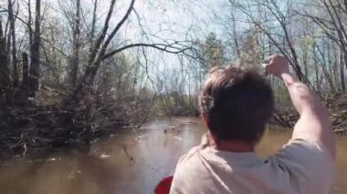 Nehirde küreği olan bir adam salda yüzüyor. Şarjör. Güneşli bahar gününde sakin, çamurlu bir nehirde yüzen bir adamın arka görüntüsü. Bahar selleri sırasında sakin bir nehirde rafting yapmak