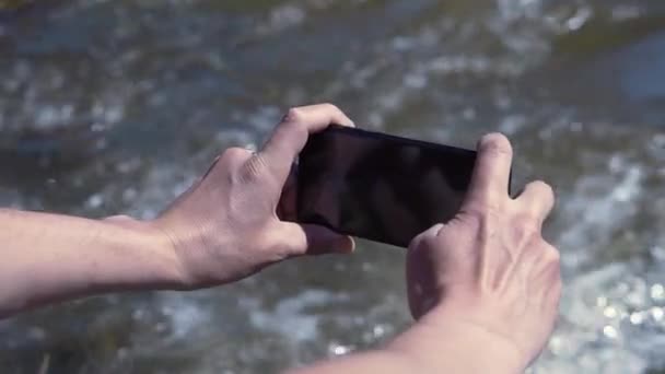 남자가 강을 핸드폰으로 찍고 있어. 클립. 진흙투성이의 강을 배경으로 핸드폰을 들고 있는 사람들 이 줄을 섰습니다. 자연계의 사람은 전화로 모든 것을 사진으로 찍는다 — 비디오