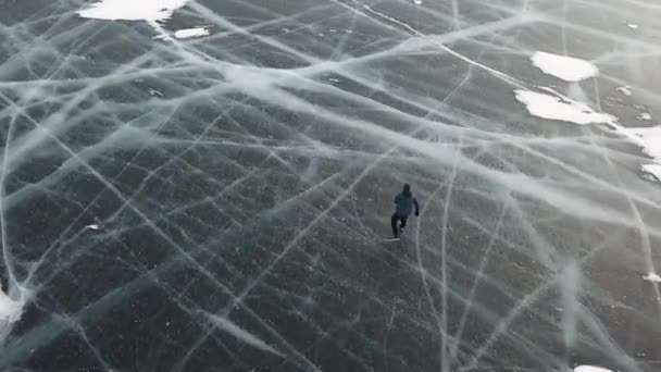 Vista aérea superior de um homem patinando no gelo ao ar livre no reservatório de água congelada. Clipe. masculino turista gelo patinação no congelado lago com espessura de gelo com profundidade rachaduras abaixo dele pernas . — Vídeo de Stock