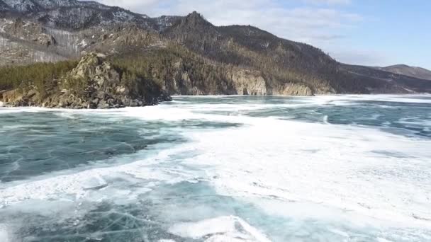 Beautiful views of a frozen winter lake with snowy forested mountains. Clip. Aerial view of frozen water reservoir of turquoise color and coniferous forest on mountain slopes. — Stock Video