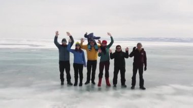 Bir grup arkadaş donmuş gölde eğleniyor. Şarjör. Buzul kaplı su deposunun kalın buzulunda duran ve kameraya el sallayan mutlu turistlerin insansız hava aracı görüntüsü.