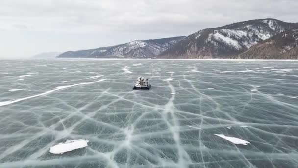 Khivus hovercraft passeios no lago congelado Baikal. Clipe. Vista aérea de um hovercraft que se move no gelo de um reservatório congelado no tempo de inverno em colinas nevadas de tirar o fôlego e fundo de céu nublado . — Vídeo de Stock