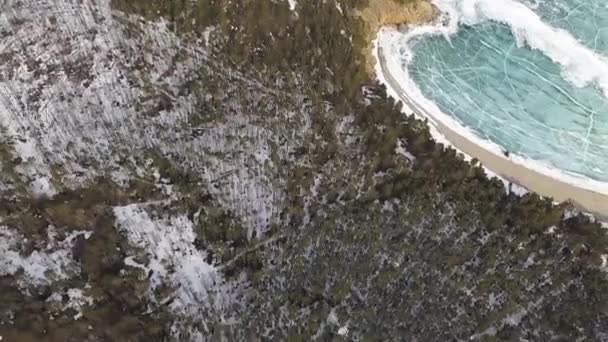 Zmrazené jezero Bajkal obklopené stromy a horami. Klip. Dech beroucí letecký pohled na zalesněné kopce a jezero s plátky ledové kry zamrzlé do tloušťky průhledného ledu. — Stock video