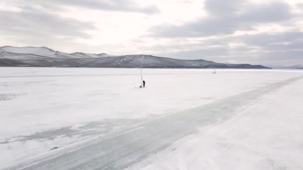 Vista aérea de um homem em pé perto do barco no lago congelado Baikal. Clipe. Voando sobre a superfície de água gelada com iates de gelo, esporte de inverno e conceito de estilo de vida ativo . — Vídeo de Stock