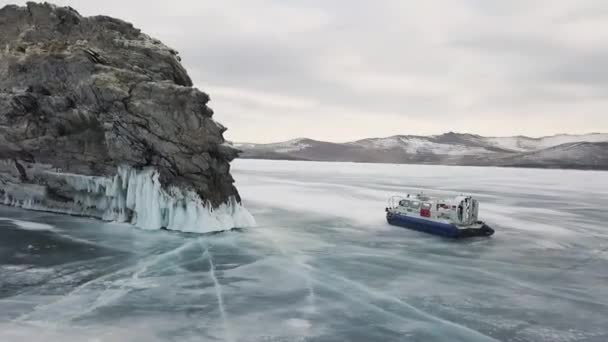Luchtfoto van een hovercraft die in een slip gaat op een ijzig wateroppervlak rond de rots. Een knip. Prachtig winterlandschap van bevroren Baikal Lake met ijskoude kliffen van Olkhon Eilanden. — Stockvideo