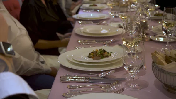 Primer plano de la mesa del restaurante servida para la cena. Imágenes de archivo. Mano de camarero poniendo un plato blanco con un plato sobre la mesa con copas llenas de vino durante el banquete . — Foto de Stock