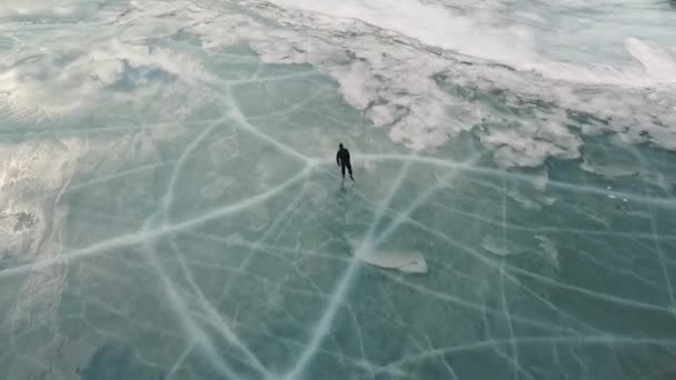 Aerial view of a man skating on lake Baikal covered by ice. Clip. Male sportsman ejoying sport in cold weather with the sky and clouds reflected in the beautiful icy surface of the lake. — Stock Video