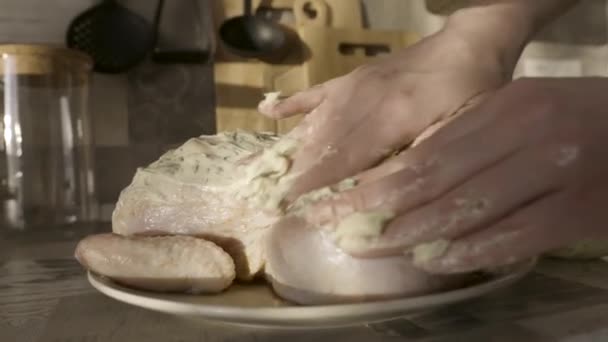 Menina marinando frango cru para cozinhar no forno. Acção. Close up de mãos femininas colocando molho de maionese com vegetação no frango cru deitado na placa na cozinha . — Vídeo de Stock