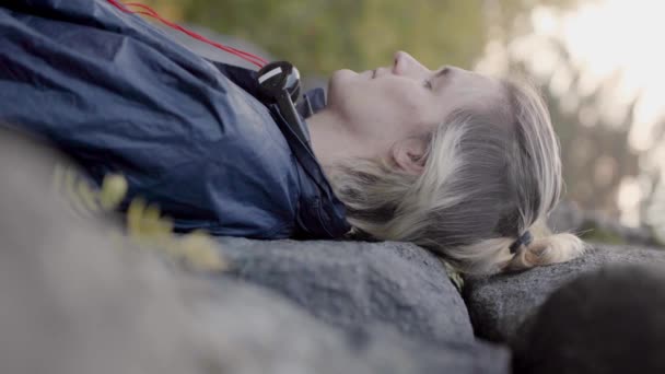 L'homme est allongé les yeux fermés sur des rochers. Des actions. Le gars sensible se trouve sur un sol en pierre dans la forêt et fusionne avec la nature. Jeune homme se relaxe dans la nature — Video