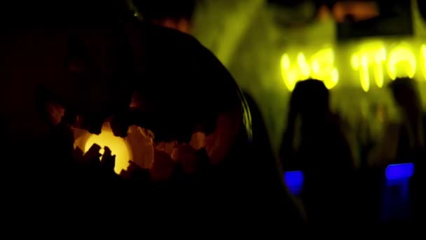 Calabazas de Halloween en una espeluznante oscuridad y luces. Imágenes de archivo. Primer plano de la calabaza de miedo con una lámpara amarilla en el interior y la gente se divierte en el fondo . — Vídeos de Stock