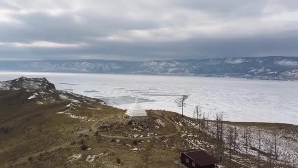 Buddhistiska dumheter på ön Ogoy vid Bajkalsjön. Klipp. Kultur och traditioner i Sibirien, vit stupa på fruset vatten i Baikal på bakgrunden, plats för gudomlig upplysning. — Stockvideo