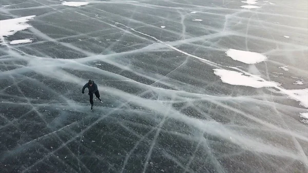 Vista aérea de un hombre patinando en el lago Baikal cubierto de hielo. Clip. Hombre deportista eyaculando deporte en clima frío en la hermosa superficie helada del lago . —  Fotos de Stock