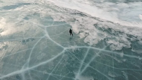 Vista aérea de un hombre patinando en el lago Baikal cubierto de hielo. Clip. Hombre deportista eyaculando deporte en clima frío con el cielo y las nubes reflejadas en la hermosa superficie helada del lago . — Foto de Stock