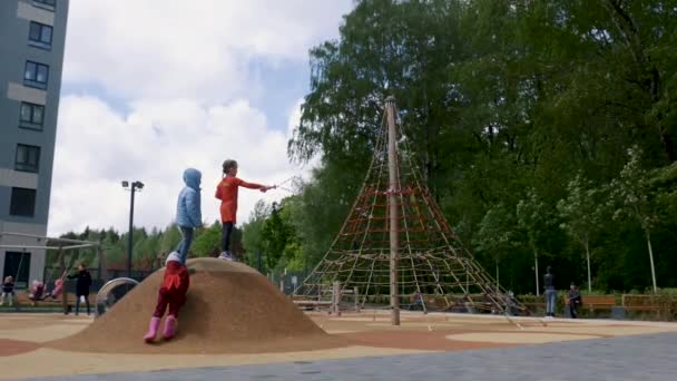 Liten flicka och hennes vänner blåser såpbubblor på lekplatsen. Börja. Barn som står på konstgjord kulle nära reppyramiden och gör såpbubblor. — Stockvideo