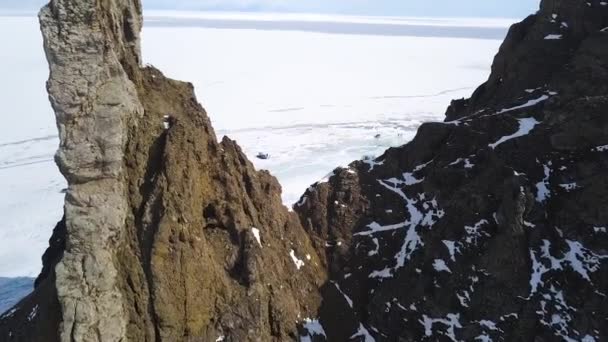 Veduta aerea di incredibili scogliere nel periodo invernale e l'infinito lago ghiacciato. Clip. Paesaggio naturale con rocce su cielo nuvoloso e fondo superficie dell'acqua ghiacciata. — Video Stock