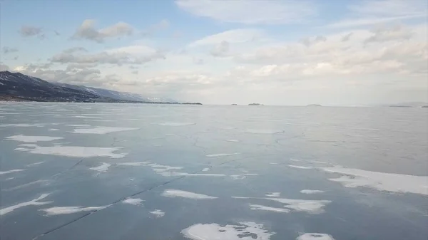 Impresionante vista aérea del lago congelado Baikal, Siberia, Rusia. Clip. Volando a través del hielo azul del depósito de agua en las montañas y el fondo azul cielo nublado . —  Fotos de Stock