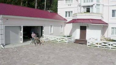 Adam bahçedeki kütüğü kesiyor. Video kaydı. Zengin kır evinin arka planındaki işçi kesme kütüğünün en üst görüntüsü. Şömine için odun kesen işçi.