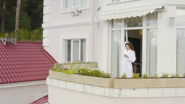 Mujer disfruta de la mañana en el balcón de la casa de campo. Vídeo. Vista superior de la mujer rica bebiendo café en el balcón de su gran casa de campo en el fondo del bosque — Vídeo de stock