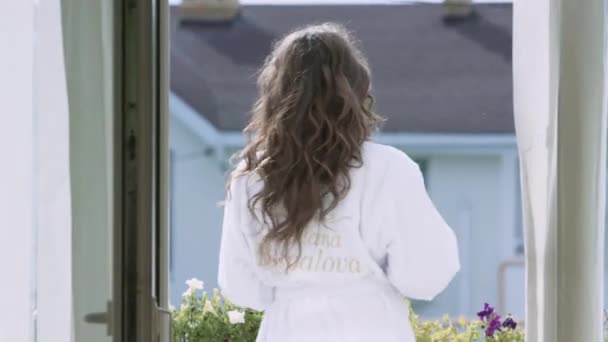 Belle femme profitant d'une matinée ensoleillée avec tasse de café sur le balcon. Vidéo. Femme attrayante en manteau blanc se détendre dans un hôtel cher et profiter d'une matinée ensoleillée — Video