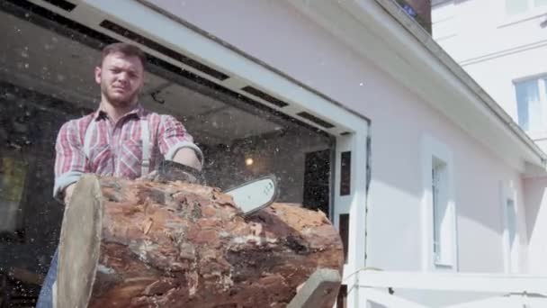 Lambat-gerak memotong log dengan gergaji. Video. Pria muda Brutal memotong sepotong kayu dengan gergaji di latar belakang garasi. Serbuk gergaji terbang ke segala arah dari melihat — Stok Video