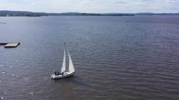 Vista superior del yate de vela que navega lejos de la orilla. Vídeo. Yate con velas blancas zarpa del muelle y se dirige hacia el horizonte. Deportes náuticos en yates de vela — Vídeos de Stock