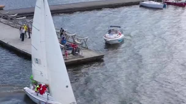 Верхній вигляд вітрильної яхти відпливає від берега. Відео. Яхта з білими вітрилами і екіпажем відпливає від пірсу. Морські види спорту на вітрильних яхтах — стокове відео