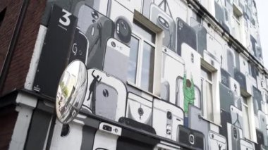 Flacon Tasarım Fabrikası 'nın dış cephesi. - Sanat. Birçok beyaz, gri ve siyah akıllı telefonun duvar yazısıyla dekore edilmiş binanın alt manzarası..