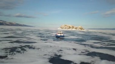 Su deposunun nefes kesen buzlu yüzeyi, kalın buzlarla bağlanmış, ve hareket eden hovercraft. Şarjör. Donmuş gölde hava yastığı aracında seyahat eden turist grubunun hava görüntüsü.