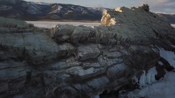 Vista aérea del acantilado con pendientes pronunciadas en el fondo de montañas boscosas y estanque congelado. Clip. Montañas con picos parcialmente cubiertos de nieve por el hermoso lago congelado Baikal bajo — Vídeos de Stock