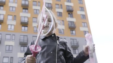 Küçük güzel kız sabun köpüğüyle oynarken heyecanlı ve mutlu görünüyor. Başla. Rüzgarlı bir havada, çok katlı evin yakınında dev kabarcıklar çıkaran sevimli çocuk..