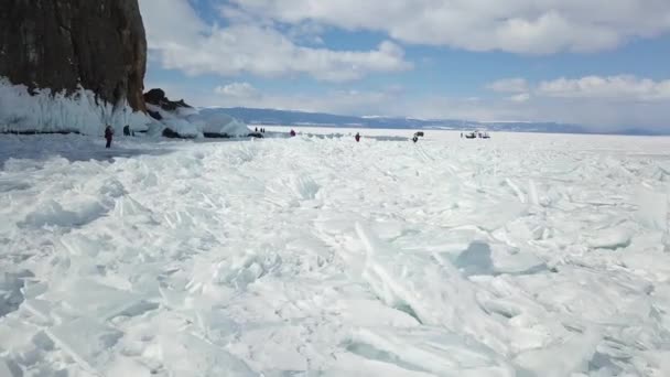 Dech beroucí pohled na lidi kráčející po popraskaném ledu jezera Bajkal v zimním období. Klip. Koncept turistiky a přírody, skupina turistů kráčejících po zamrzlém jezeře v blízkosti útesu. — Stock video