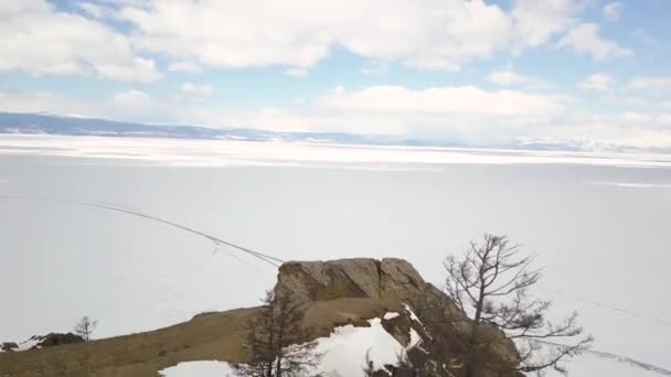 Steile rots en de oever van een bevroren meer. Een knip. Uitzicht vanuit de lucht op de steile klif en bergen bedekt met kale bomen en het meer onder het ijs en sneeuw, winter natuur landschap. — Stockvideo