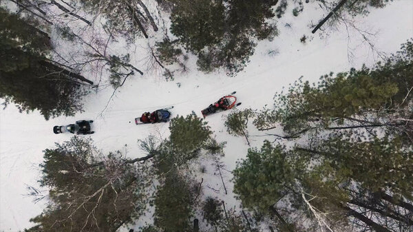 Aerial top view of a team stopped while traveling in the winter woods on snowmobiles. Clip. The sportsmen on snowmobiles ready to move through deep snowdrifts in the winter forest.