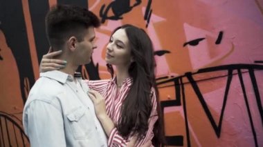 Sokakta sarılan genç ve şık bir çiftin oldukça güneşli açık hava portresi. Başla. Romantik genç çift, açık havada buluşuyor nazikçe sarılıyor ve flört ediyor, aşka bakıyor, aşk hikayesi kavramını anlatıyor..