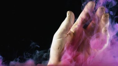 Yapay elin etrafına yayılan pembe parlak mürekkep bulutunu kapat. Stok görüntüleri. Siyah arkaplanda izole edilmiş el figürü ve boyalar.
