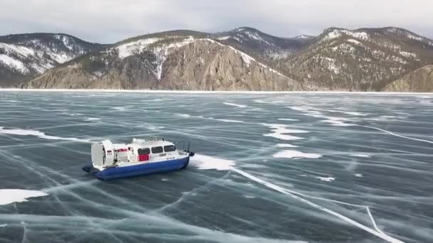 Hovercraft beweegt op een vlak sneeuw- en ijsoppervlak. Een knip. Luchtfoto van het reddingsluchtkussenvoertuig dat in de winter langs de bergachtige oever van het bevroren meer beweegt. — Stockvideo