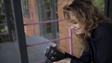 Profesyonel kameralı kadın fotoğrafçının portresi. Başla. Beyaz kadın, kıvırcık saçlı, kırmızı tuğlalı arka planda fotoğraf çekiyor..