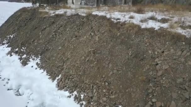 Luchtfoto van een geruïneerd gebouw gelegen op de helling van een berg in de buurt van het bevroren meer. Een knip. Vliegen over verlaten bakstenen huis gebouwd op beboste heuvel in de winter seizoen in de buurt van ijzige rivier. — Stockvideo