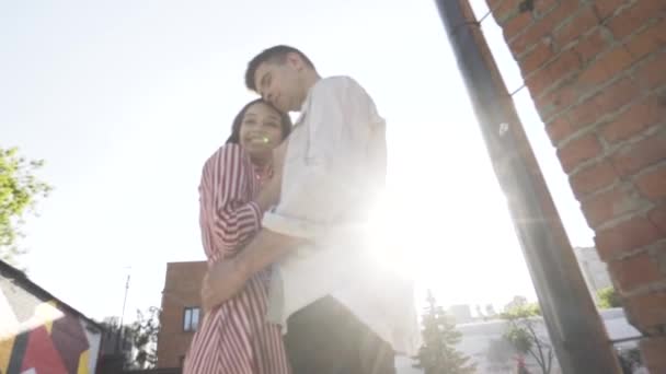 Zamilovaní muži a ženy se objímají na ulici. Akce. Šťastný kavkazský mladý pár objímající a usmívající se venku proti jasnému slunečnímu svitu, dolní pohled. — Stock video