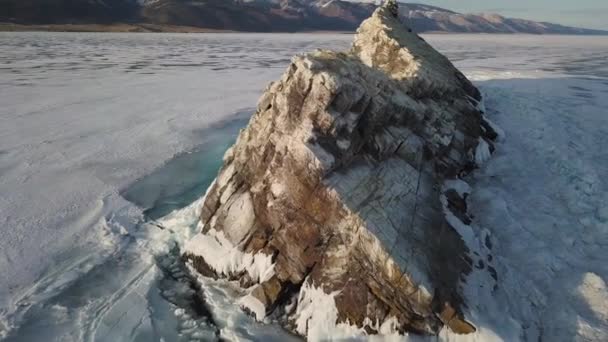 Vue aérienne de la falaise enneigée sur le réservoir d'eau gelée. Clip. Eau gelée du lac Baïkal et surface glaciaire de glace avec fissures, fissures et bancs de neige et littoral pierreux avec rochers et falaises. — Video